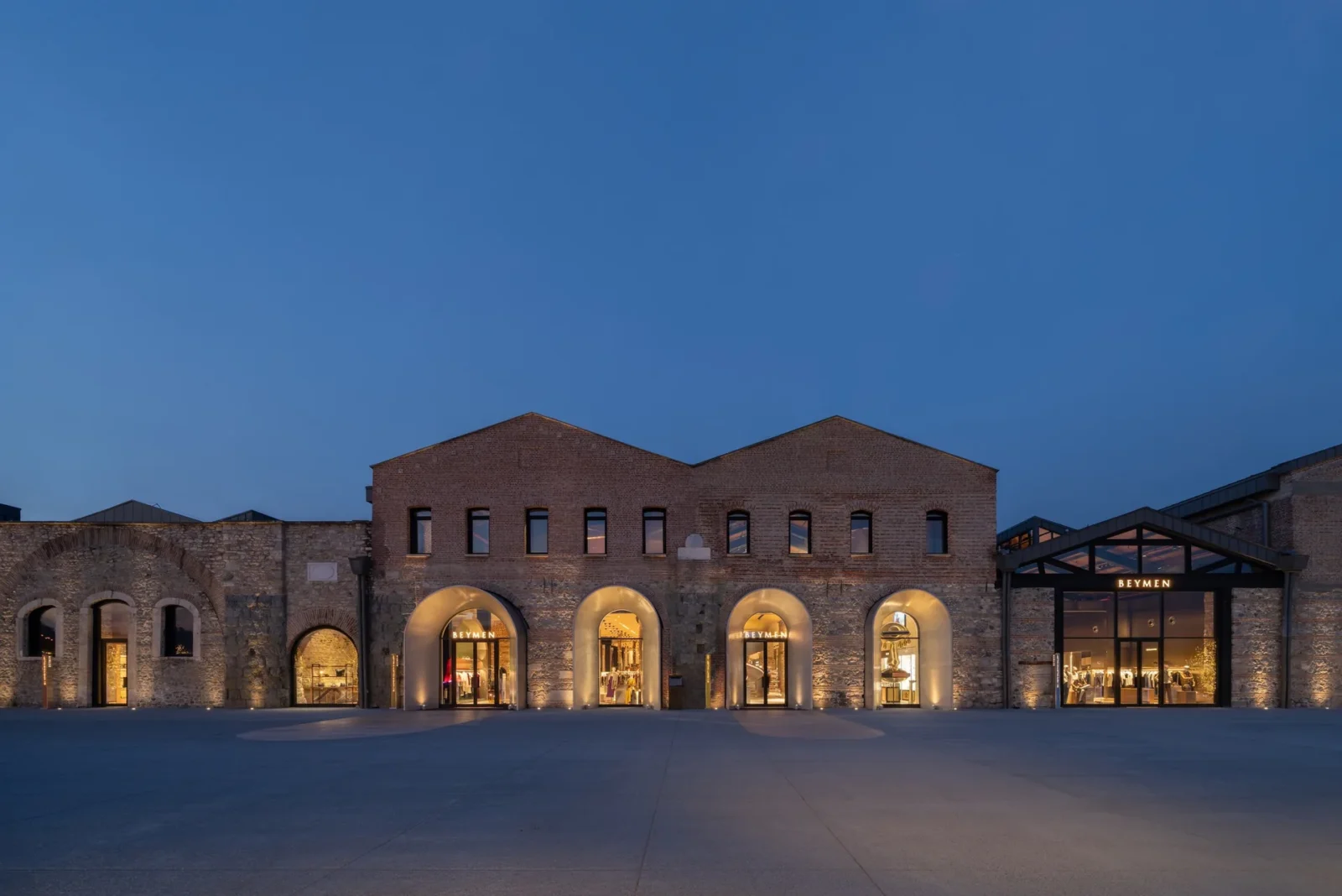 Beymen Tersane by OMA, the brick shipyard halls lit through their arches at dusk