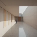 Wide daylit corridor in a public building with terrazzo floor, tall flush doorways and a person walking in the distance