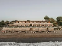 The beach elevation of Dexamenes Seaside Hotel with loungers in front of it