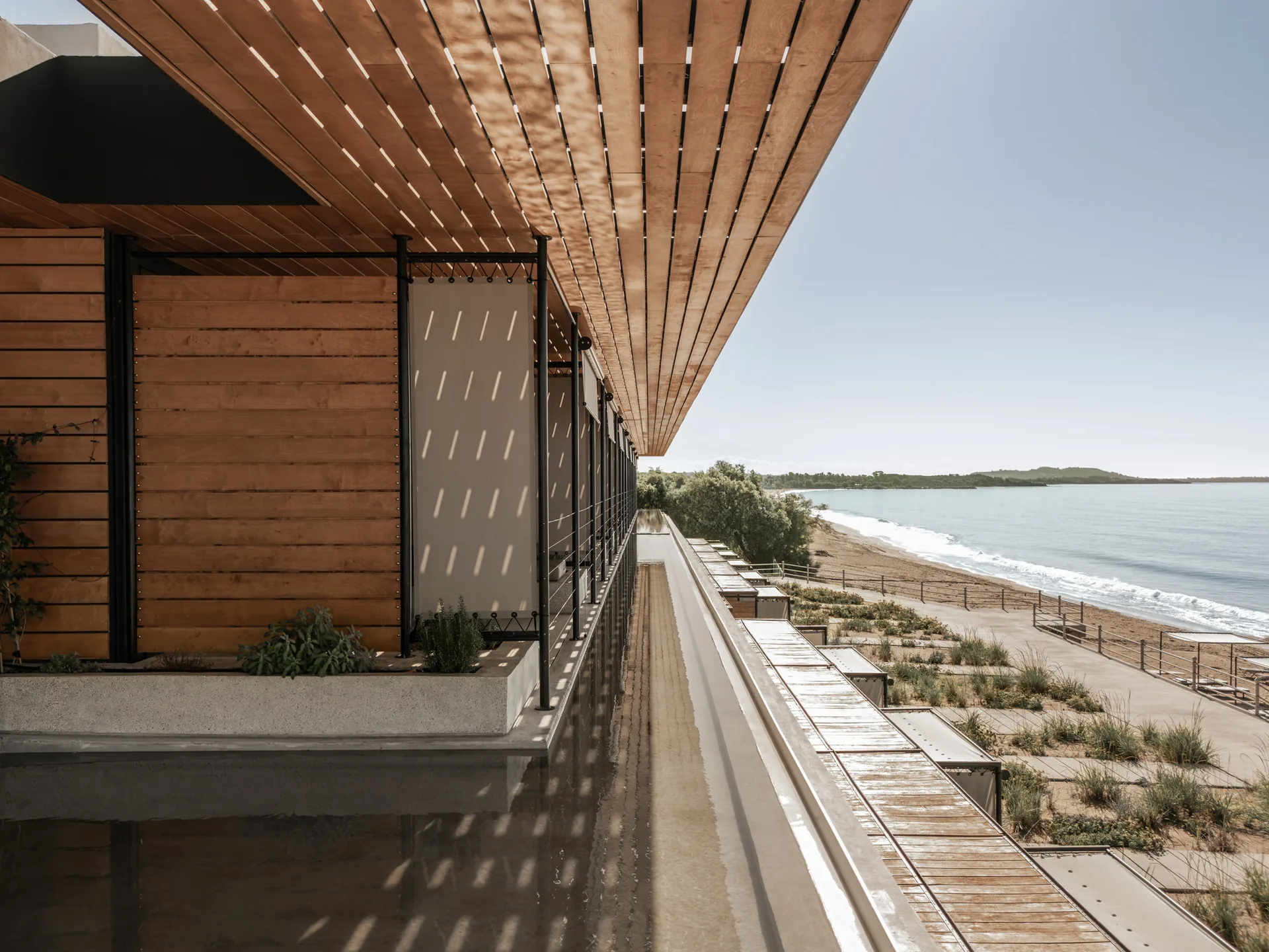 The timber pergola casting shadows toward the sea at Dexamenes Seaside Hotel