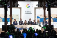 Officials clap on stage under a screen reading 'Investing in Finland' with the Google logo, confetti falling