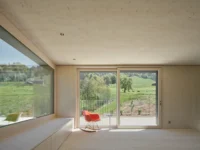 Living room lined in timber with the meadow beyond, House on Concrete Walls