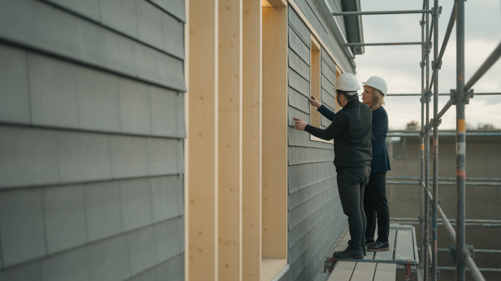 Two people in hard hats examining a junction detail on a partly clad facade