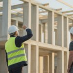 Architect in a hard hat on a construction site looking up at the rising concrete frame