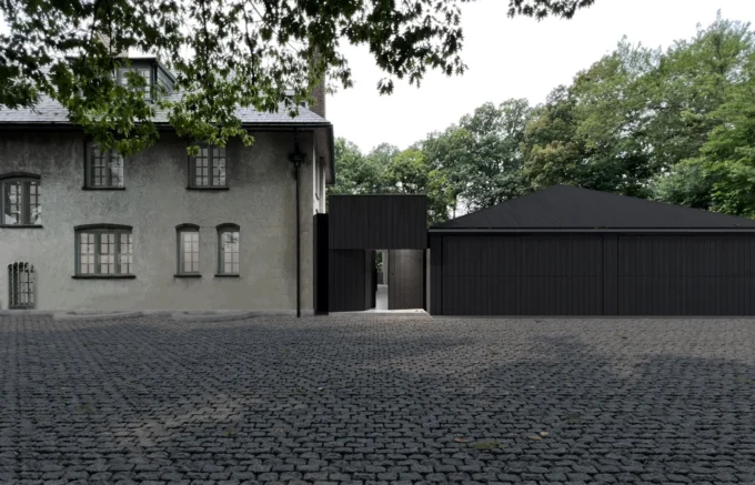Blackened timber garage addition beside the historic Howard Van Doren Shaw house, seen across the cobbled forecourt