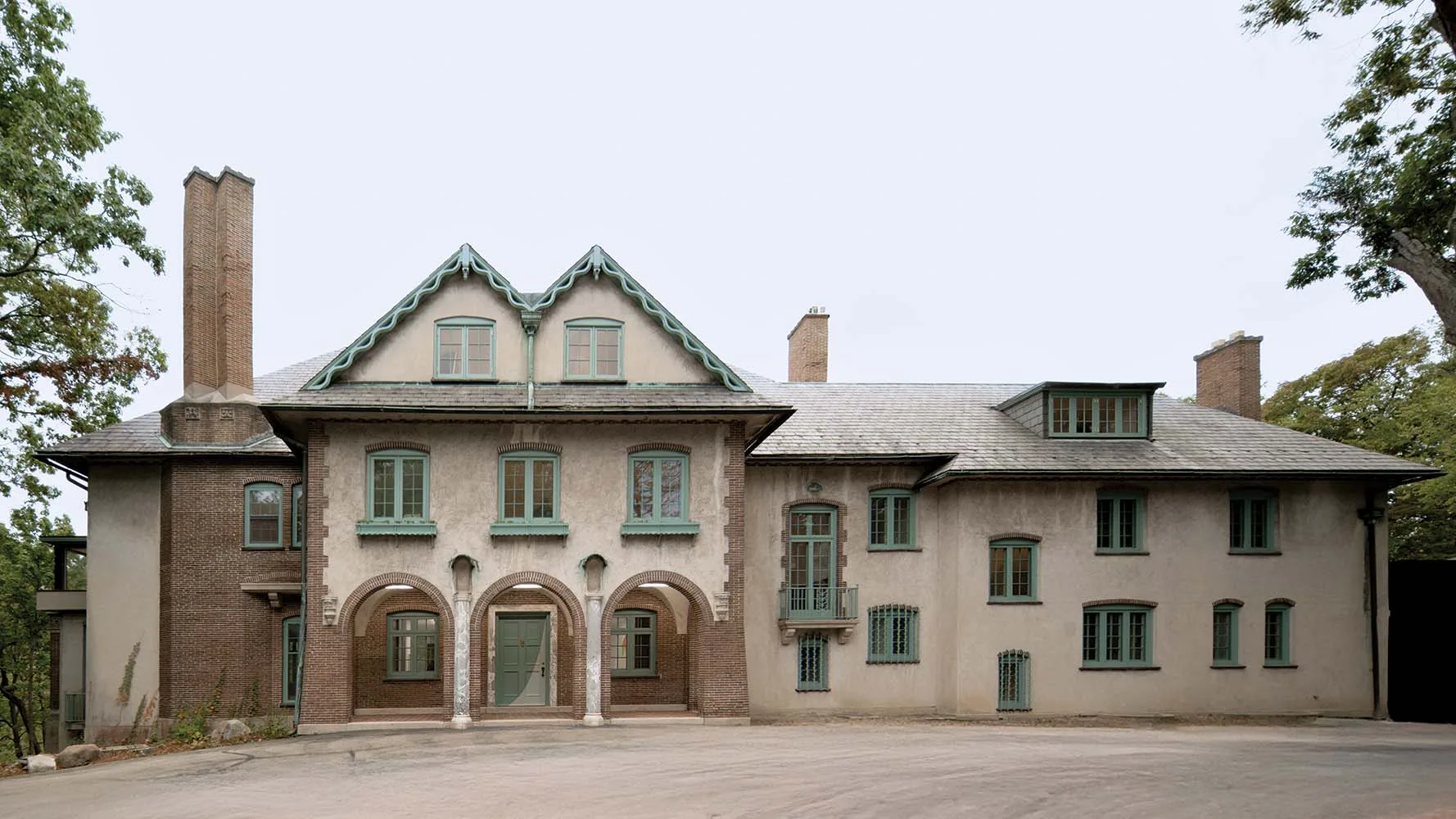 Two-story stucco and brick house with peaked gables and green-trimmed windows, arched entry porch