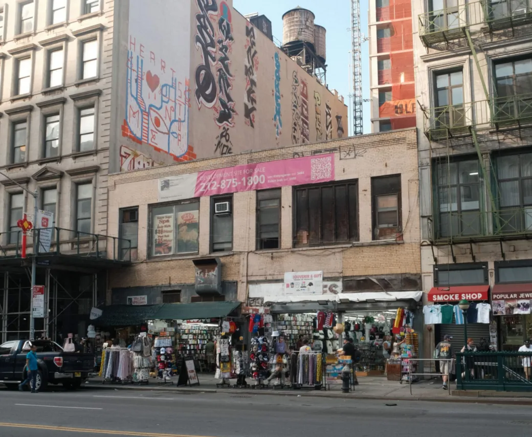 Low brick building with graffiti mural, water tanks and a street-level shop with sidewalk racks of goods