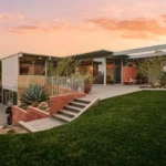Mid-century modern Adelman Residence at dusk with glass walls, a lawn and brick planters under a pink sky