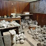Room of an architectural salvage store with stone finials, balusters and carved fragments stacked on tables and the floor