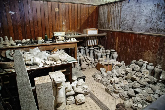 Room of an architectural salvage store with stone finials, balusters and carved fragments stacked on tables and the floor