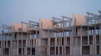 Concrete and steel building frame at dusk with repeating structural bays, separate trades working on different levels