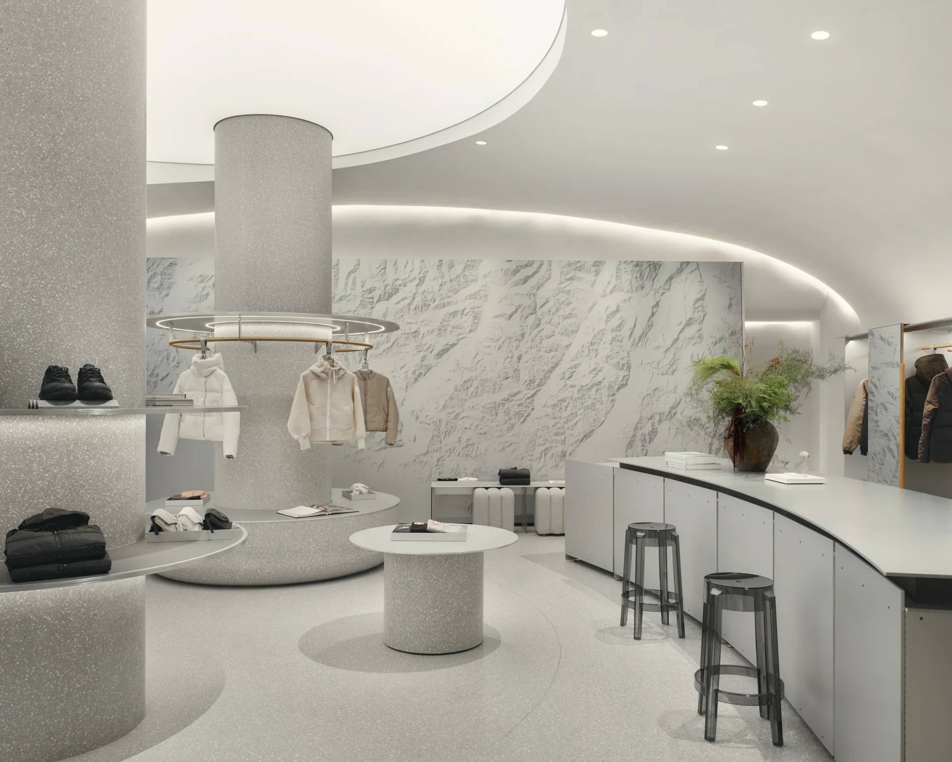 The textured white wall with plants, service counter and stools alongside