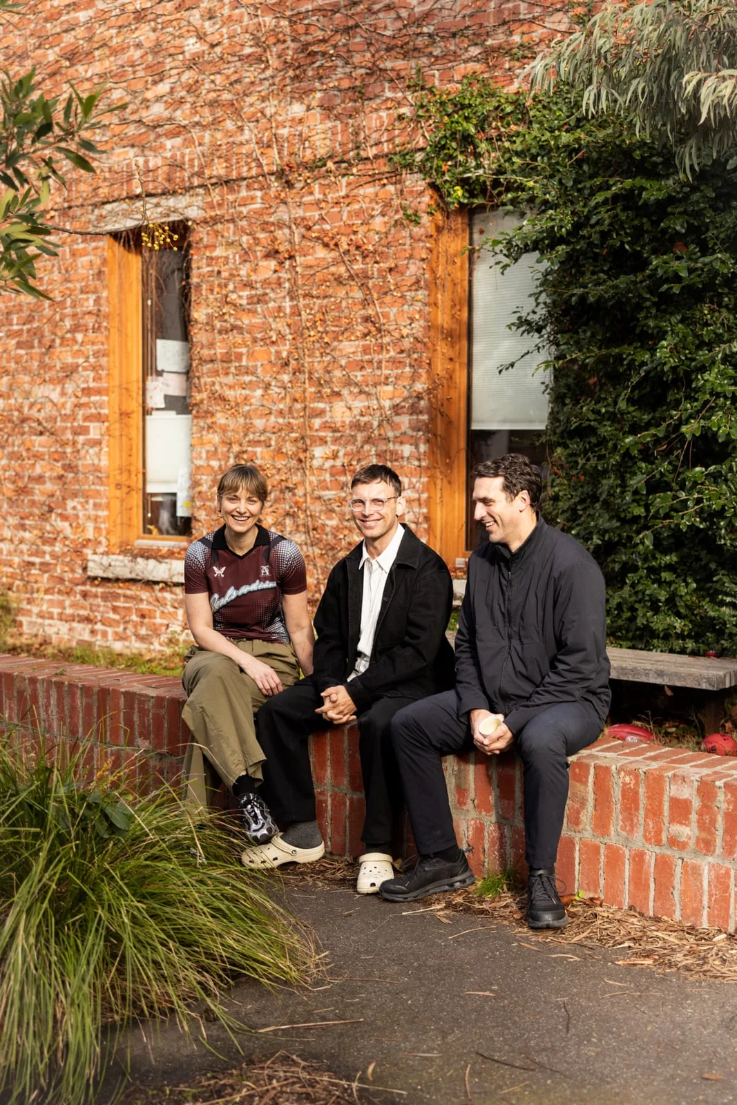 Three residents sitting on a low brick wall outside the brick townhouses of the Davison Collaborative in Brunswick