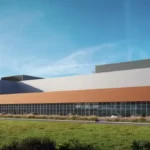Rendering of a large industrial building with orange and gray facade under a blue sky