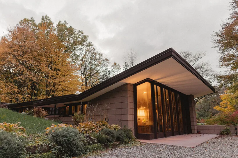 Low-slung house with a sweeping flat roof and glass windows glowing from interior light at dusk