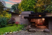 Single-story home with a low, angled overhanging roof and patterned concrete block walls, surrounded by autumn trees