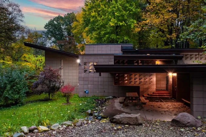 Single-story home with a low, angled overhanging roof and patterned concrete block walls, surrounded by autumn trees