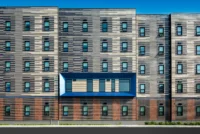 Multi-story building facade with dark and light striped brick panels and a projecting blue-framed window bay