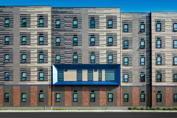 Multi-story building facade with dark and light striped brick panels and a projecting blue-framed window bay