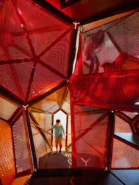A child inside a red mesh climbing volume framed by steel struts