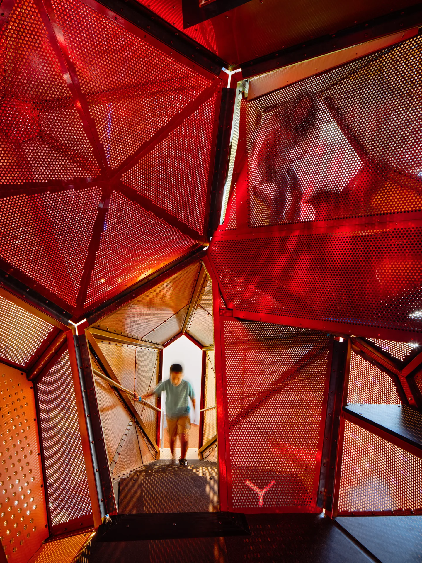 A child inside a red mesh climbing volume framed by steel struts