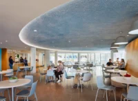 Cafe with tables and chairs under a curved ceiling beside the glazing