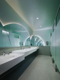 Washroom lined in green tile with an arched mirror above the basins