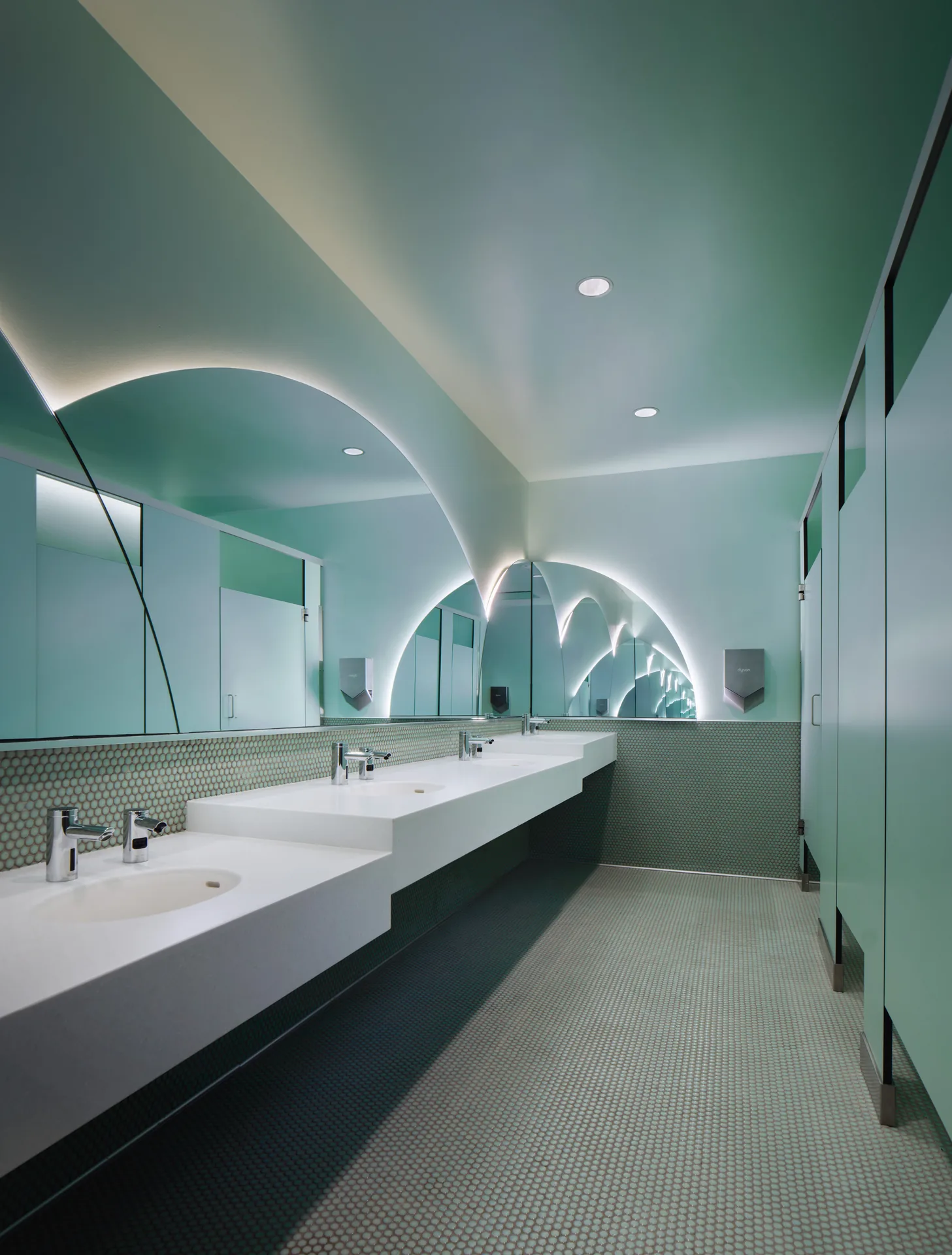 Washroom lined in green tile with an arched mirror above the basins