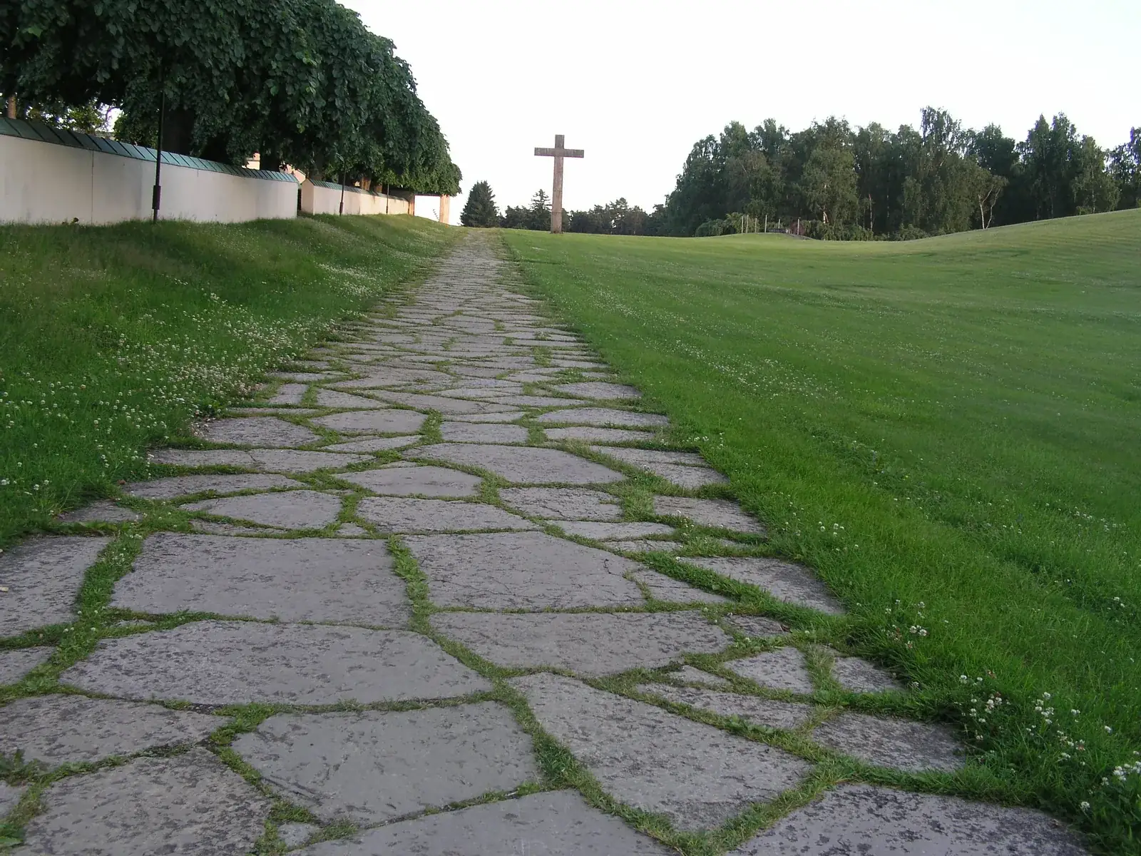 Stone path at Skogskyrkogården, the Woodland Cemetery in Stockholm, running along the wall with the granite cross in view