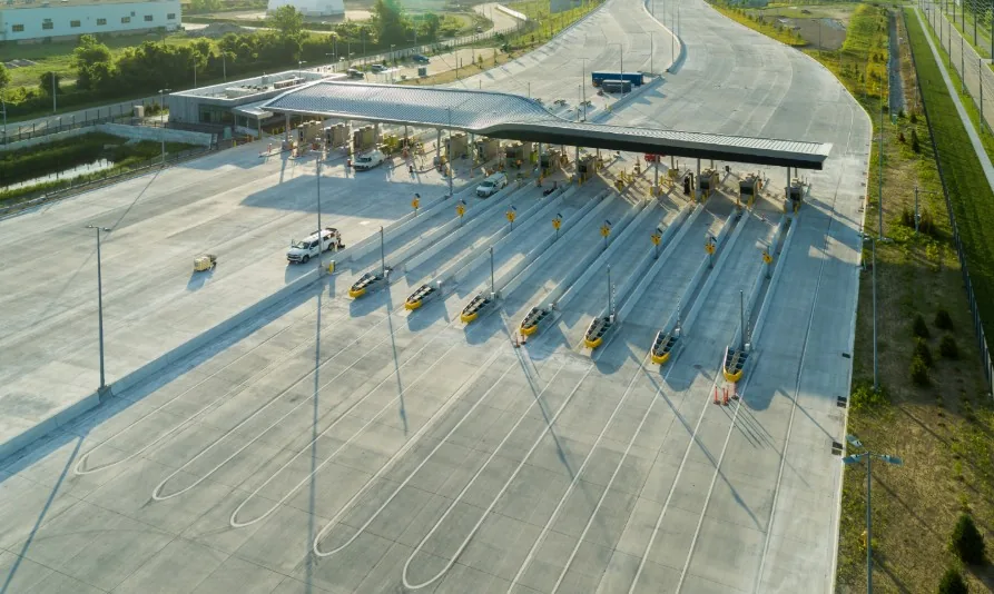 Empty multi-lane toll booth plaza with a long canopy roof and a few vehicles passing through