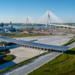 Aerial view of a cable-stayed bridge over a river with a large toll plaza and canopy on the near shore