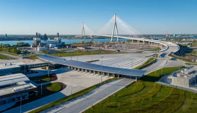 Aerial view of a cable-stayed bridge over a river with a large toll plaza and canopy on the near shore