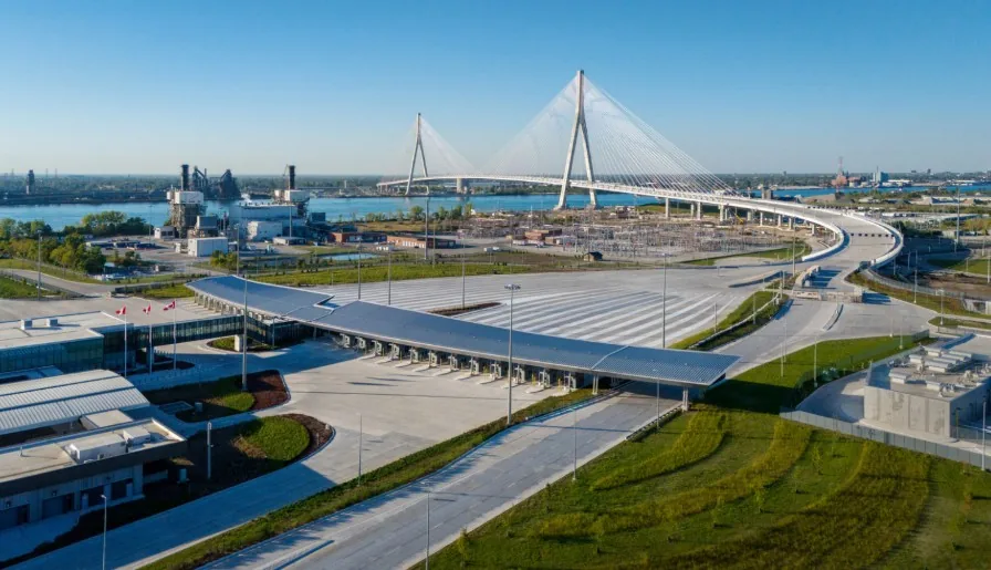 Aerial view of a cable-stayed bridge over a river with a large toll plaza and canopy on the near shore