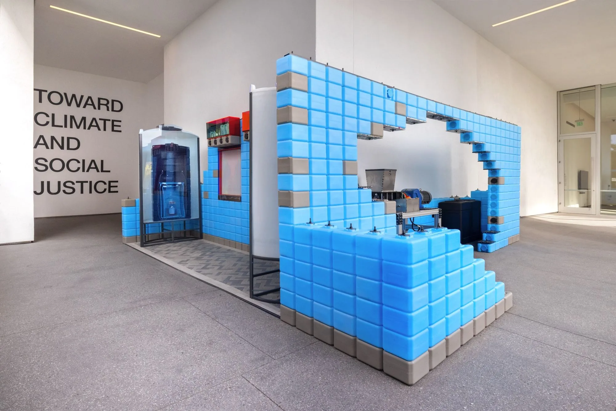 Blue modular block installation with embedded machinery beside a wall reading 'Toward Climate and Social Justice'