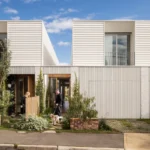 Wide view of two white townhouses with a person standing in each neighbouring yard