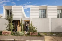 Wide view of two white townhouses with a person standing in each neighbouring yard