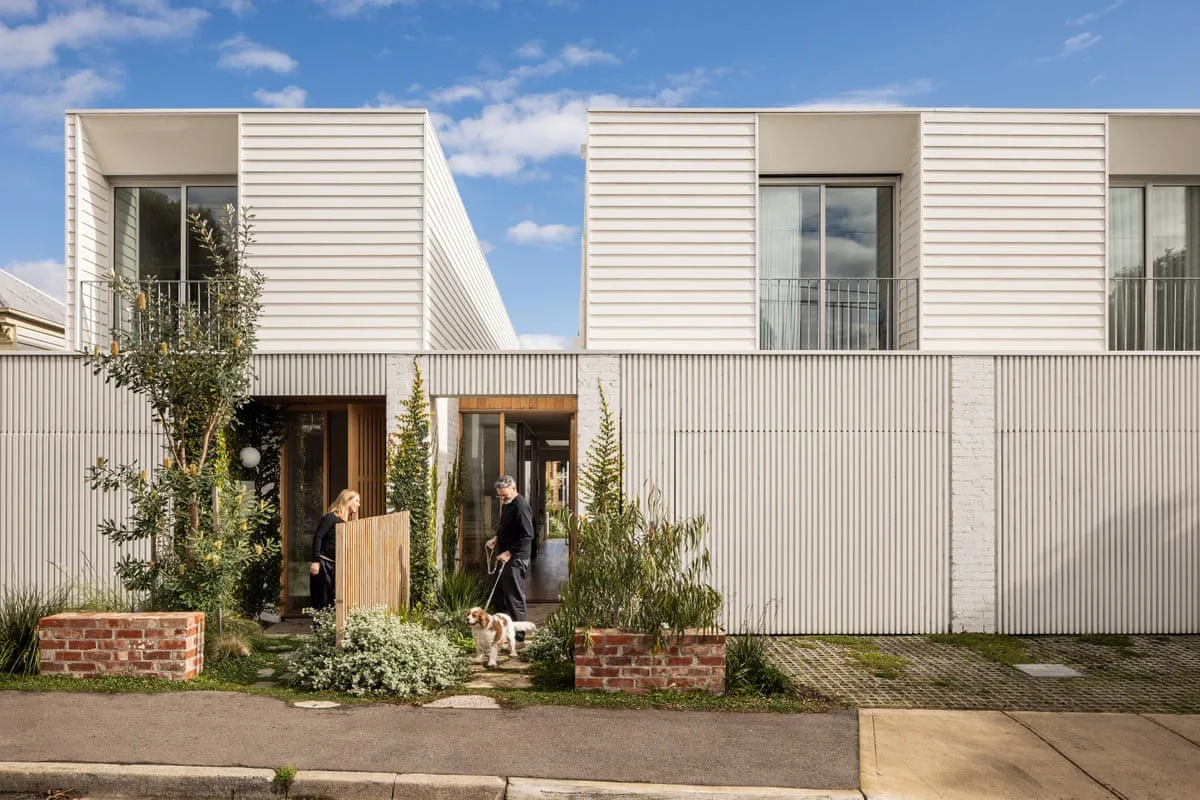 Wide view of two white townhouses with a person standing in each neighbouring yard