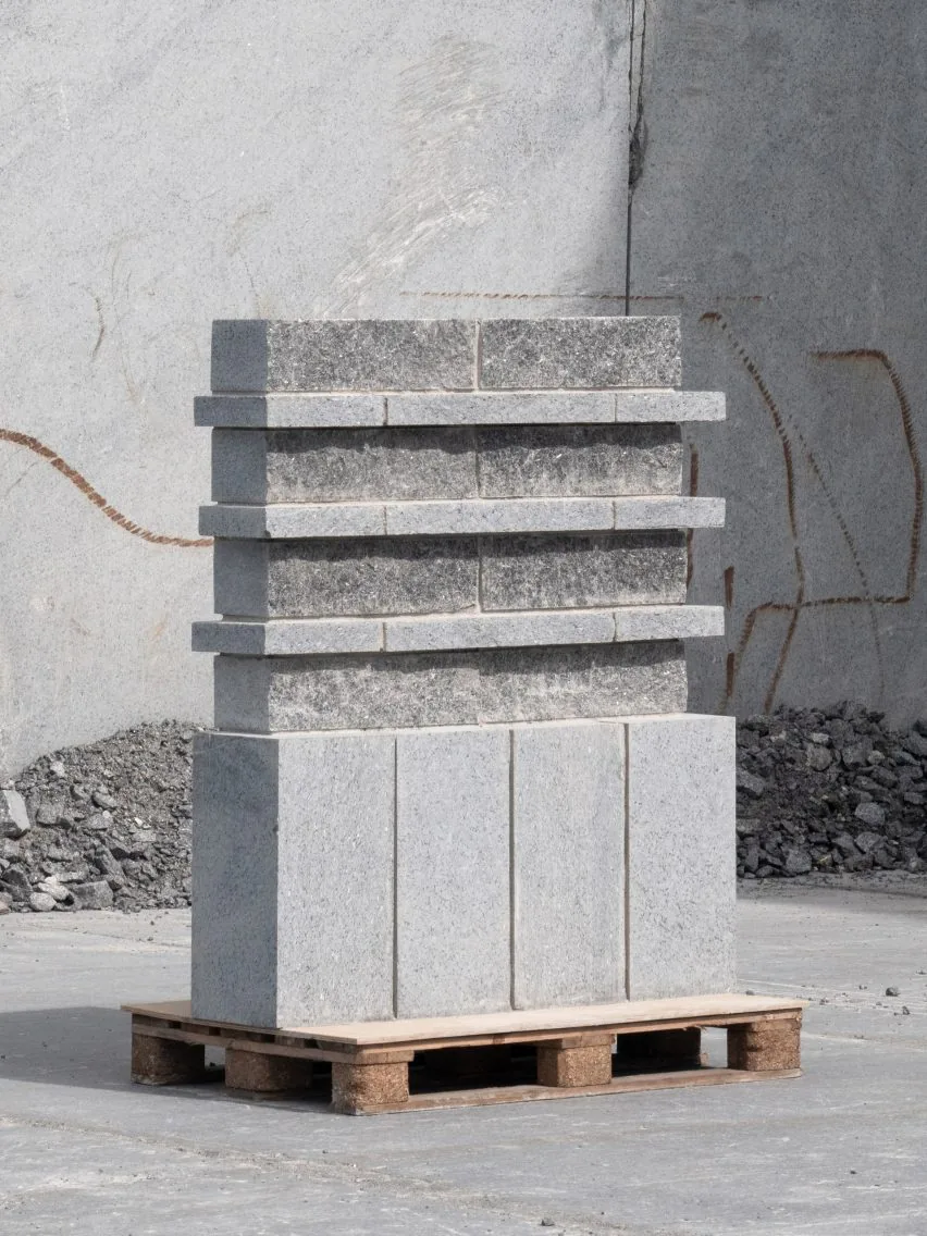 A stack of gray stone blocks arranged in layered rows sits on a wooden pallet in a quarry