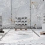 Three sculptural stacks of stone blocks on pallets stand in a quarry with rough rock walls