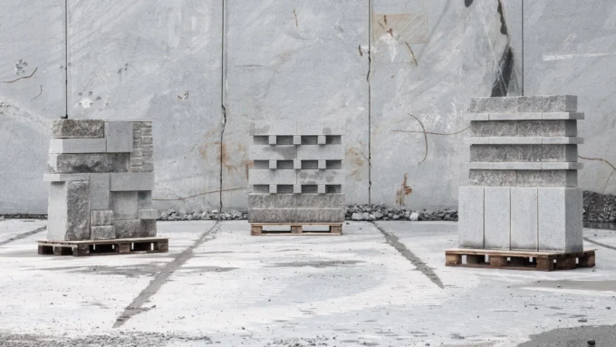 Three sculptural stacks of stone blocks on pallets stand in a quarry with rough rock walls