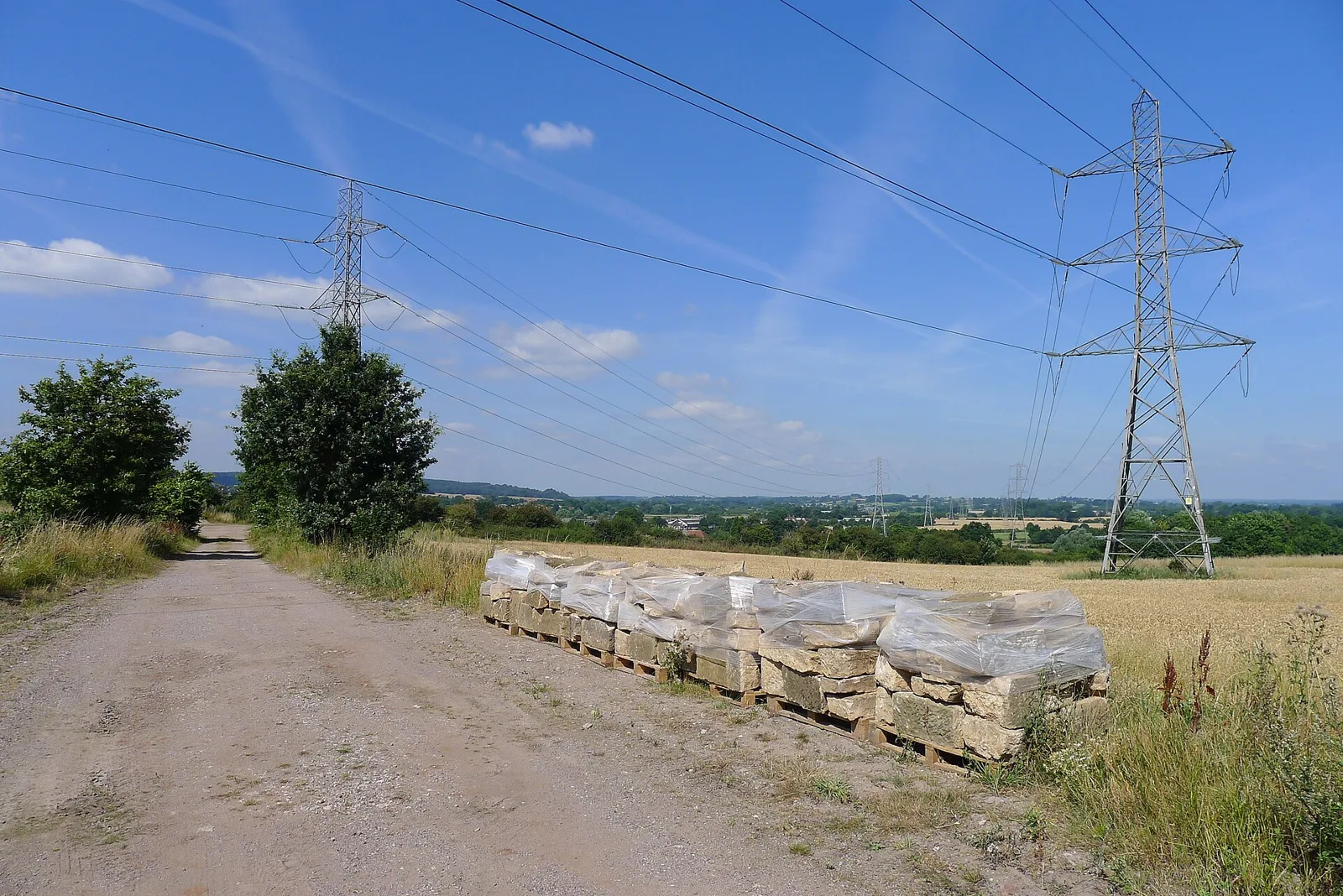 Pallets of reclaimed building stone wrapped in plastic beside a farm track under power lines