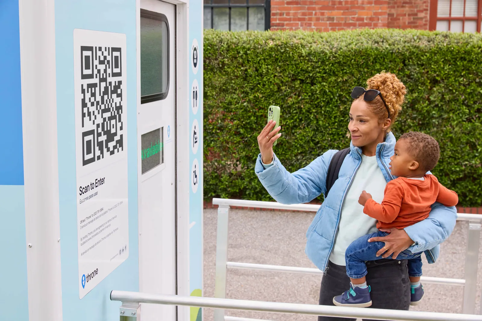 Adult with a baby scanning a QR code to unlock a freestanding public restroom unit