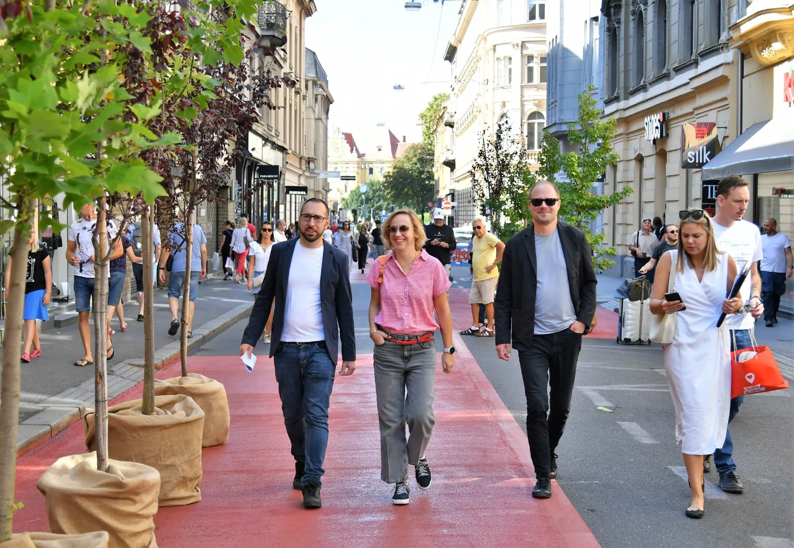 Group of people walking on a red pedestrian path lined with trees