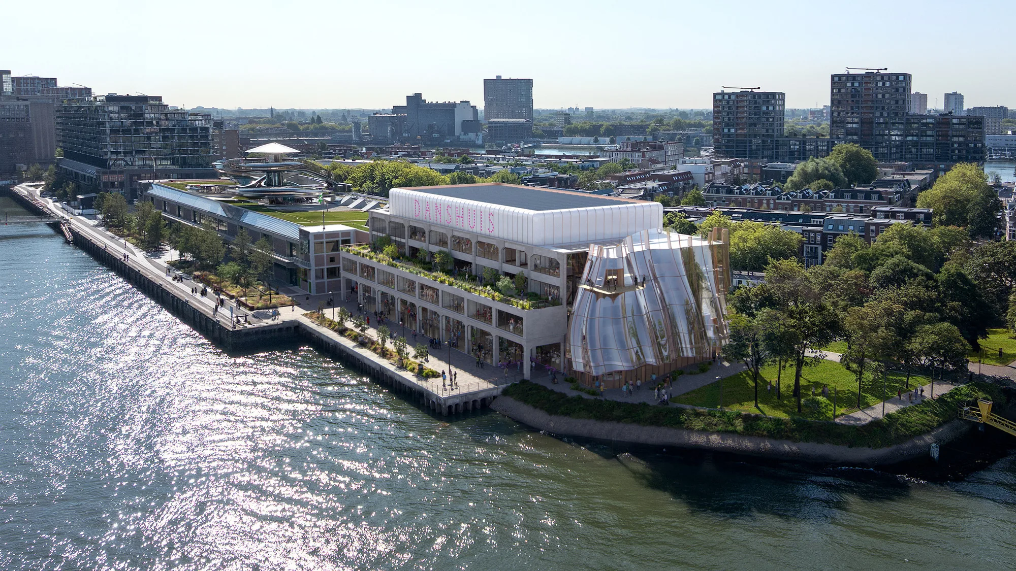 Aerial view of a waterfront building with a rippled glass facade beside a riverside park and city skyline