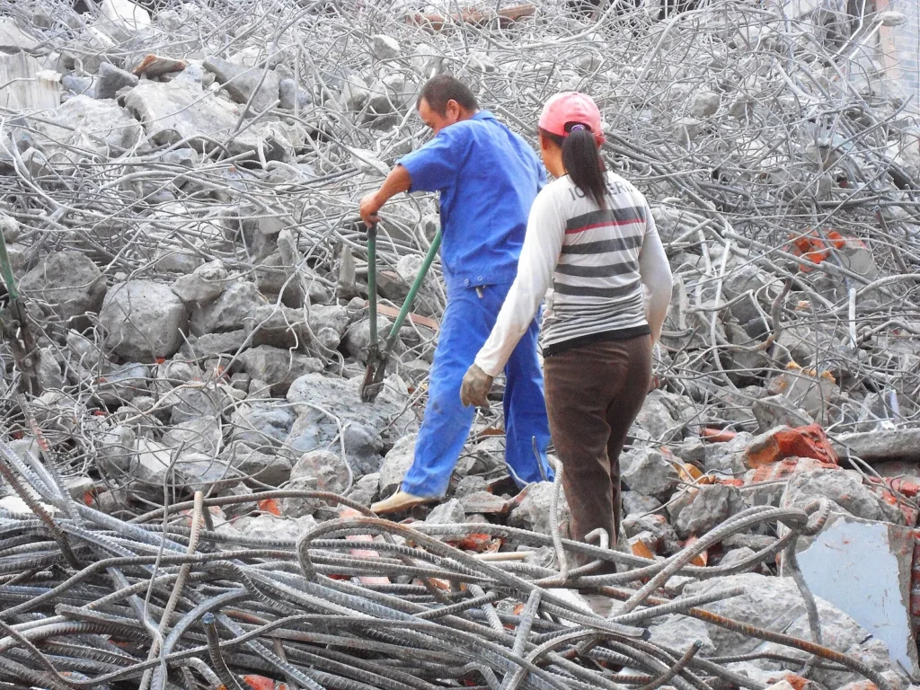 Two workers pulling steel reinforcing bars out of concrete rubble at a building demolition site