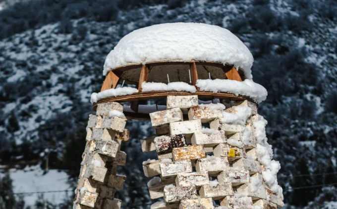 Snow-dusted mycelium block tower with mesh roof against a forested mountainside