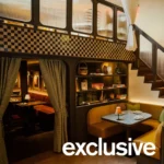 Curved booth seating with striped curtains beneath a checkered-tile mezzanine and staircase
