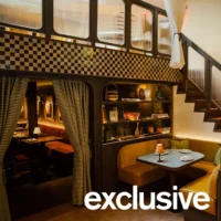 Curved booth seating with striped curtains beneath a checkered-tile mezzanine and staircase