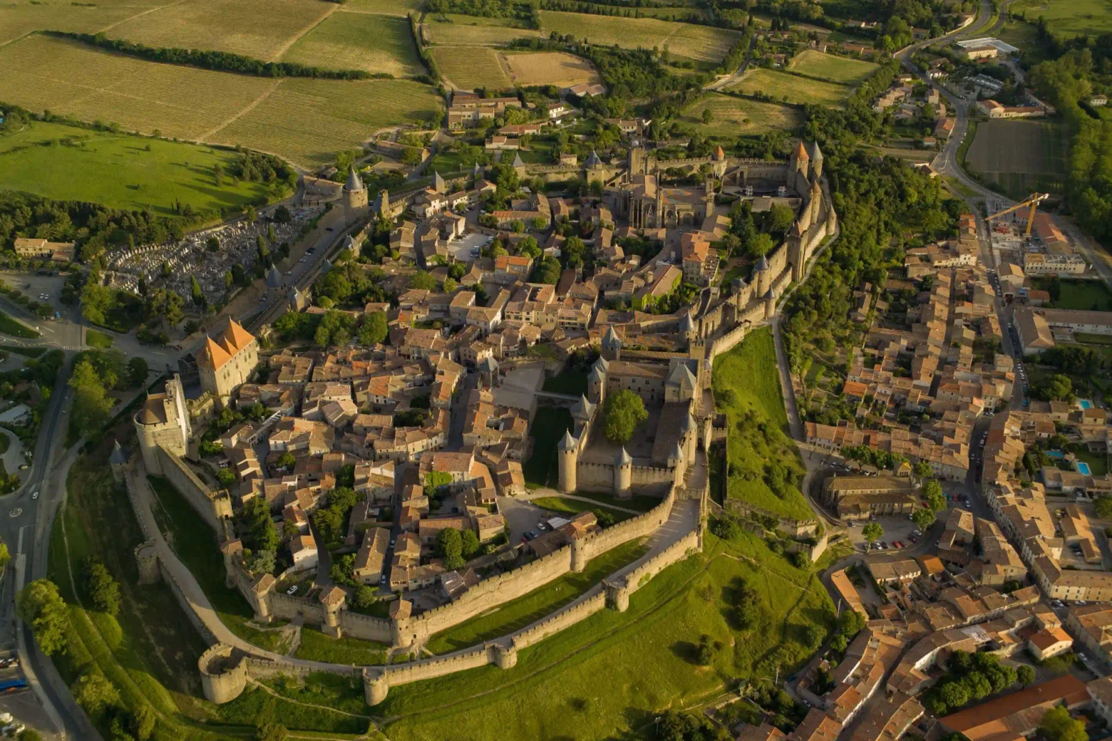 Aerial view of a walled medieval hilltop town with double stone ramparts and turrets amid green countryside