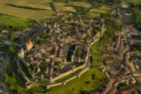 Aerial view of a walled medieval hilltop town with double stone ramparts and turrets amid green countryside